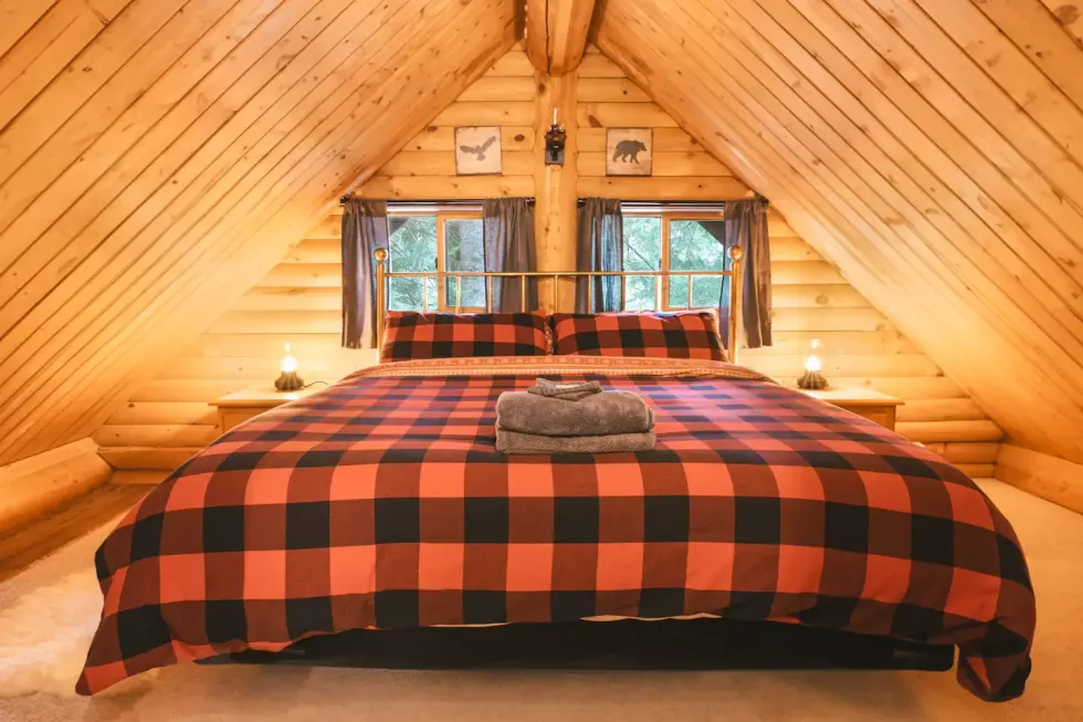 A checkered red and black duvet on a bed in a wooden cabin with towels on the bed.