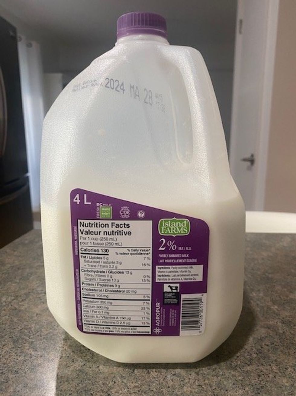 \u200bA 4-litre jug of 2% milk with a white and purple label that says Island Farms on it sitting on a brown and grey speckled kitchen counter.